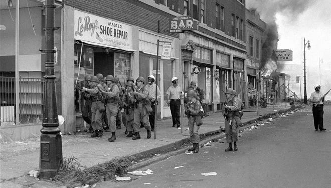 National Guardsmen with machine guns and rifles block off 12th Street on Detroit's West Side, July 26, 1967, to give firemen a chance to fight a small fire. Snipers have taken a heavy toll among firemen as they fought hundreds of fires set by rioters.