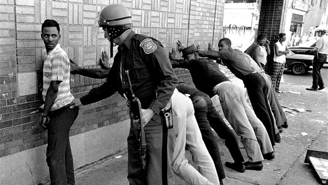 In this July 24, 1967 file photo, a Michigan State police officer searches a youth on Detroit's 12th Street where looting was still in progress after the previous day's rioting.