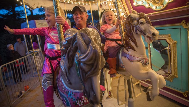 Kaia Amundsen, 5, of Des Moines, left, waves to her mom, while riding the carousel with her dad, Chris, and sister Harper, 2, while trick-or-treating during Night Eyes at Blank Park Zoo in Des Moines, Iowa, Thursday, Oct. 15, 2015.