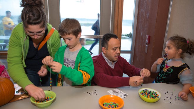 Ashley Guzman (from left), Carson Guzman, 7, both of Norwalk, Sherif El-Mahdy and Noor El-Mahdy, 5, of West Des Moines, make bracelets Friday, Oct. 23, 2015, during Halloween Hoopla at Raccoon River Park in West Des Moines.