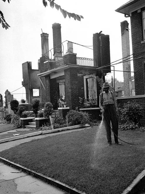 Walter Evans, who lives on Pingree St. on Detroit’s West Side, patiently waters his lawn, July 27, 1967 to keep it green in front of his home which was spared from fires set by rioters. Next door are the stark ruins of his neighbor’s home burned by a fire that swept almost the whole residential block.