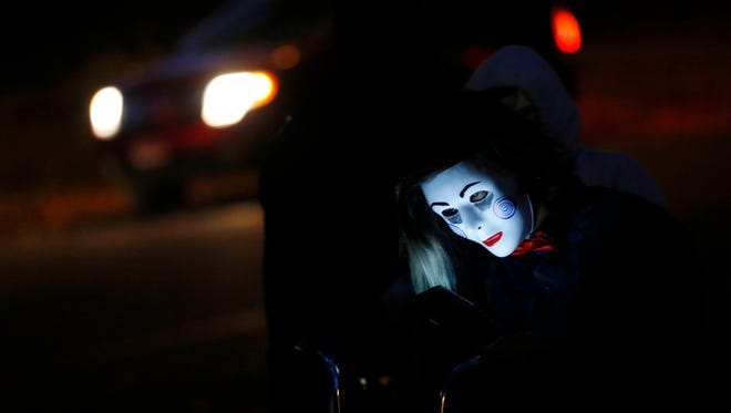 Noemi Munoz, 12, checks her phone Friday, Oct. 30, 2015, as she rides her bike along the sidewalk wearing a "Saw" mask during Beggars' Night in Des Moines.