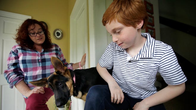 Susan Grenon chats with her son, Pauly, as their pet German shepherd, Ginger, looks on in an entryway to their home, in Smithfield, R.I. Guenon makes sure her son is lathered with sunscreen before he leaves for school in the morning, but the red-headed 10-year-old can't bring a bottle to reapply it without a doctor's note.