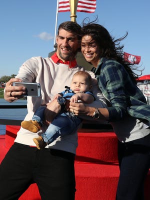 23-time Olympic gold medalist Michael Phelps and wife Nicole Johnson pose for a selfie with their son Boomer next to a giant version of the Ryder Cup trophy at Hazeltine National Golf Club.