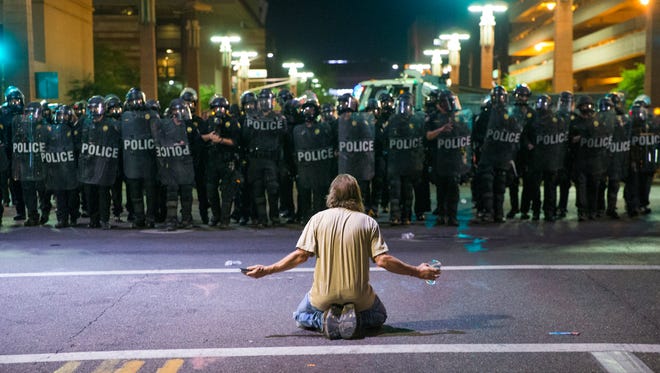 A protester sits on Second Street in front of a line of Phoenix police officers trying to clear the area after they fired gas into the crowd on Aug. 22, 2017.