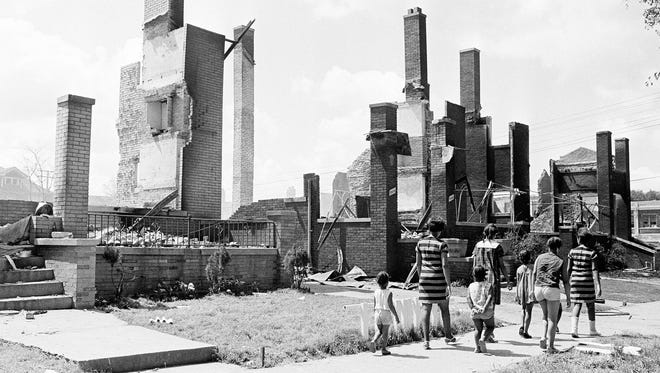 A woman and children stroll past the remains of once substantial homes which were caught up in the path of the rioters in Detroit, July 25, 1967. The houses are a short distance from 12th Street, center of the riot area.