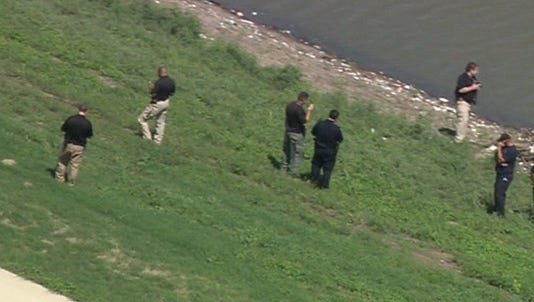 Law enforcement officers examine the scene where a body was found washed ashore at the Trinity River levee in Dallas Aug. 24, 2016.